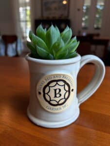 Cream colored mug filled with green plant on wooden table. 
