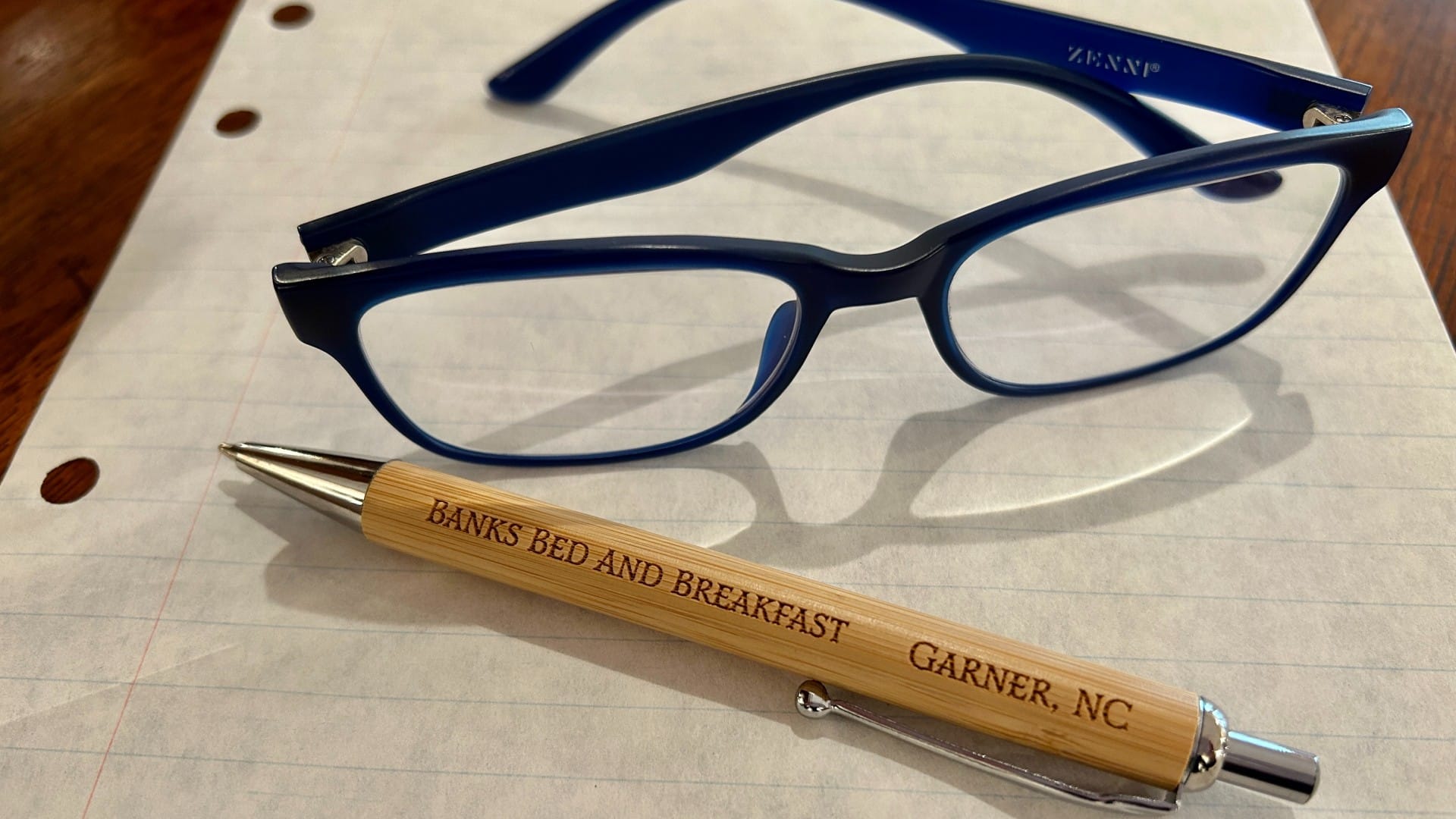 A pair of reading glasses next to a pen on an empty lined piece of paper