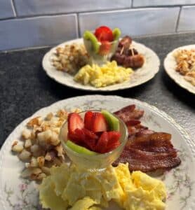 Breakfast foods of eggs, bacon, potatoes, and strawberries on a plate.