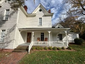 White two story house with front porch. Brick sidewalk in foreground leads to porch.