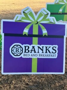 Sign shaped like a purple present with a green ribbon. Banks Bed and Breakfast written in black. 