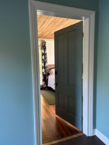 Blue door open to room with edge of bed showing.