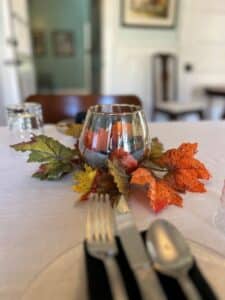 Glass surrounded by orange, green and yellow leaves next to a table setting. 