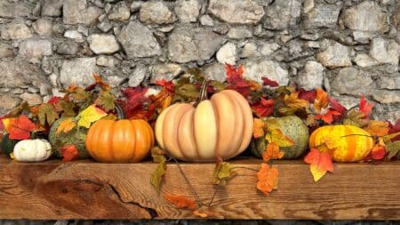 Orange and green pumpkins on wooden mantle in front of stone.