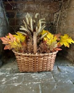 Basket with yellow and brown leaves on grey stone floor. 