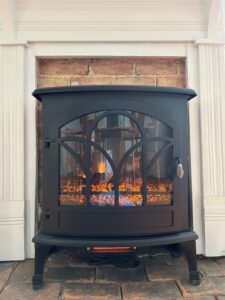 Black electric fireplace in front of brick and white wall.