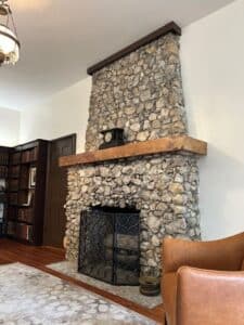 Rock fireplace with clock on the mantle. Leather chair in foreground and bookcase in background.