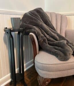 Grey blanket on chair next to small table with grey coffee mug. 