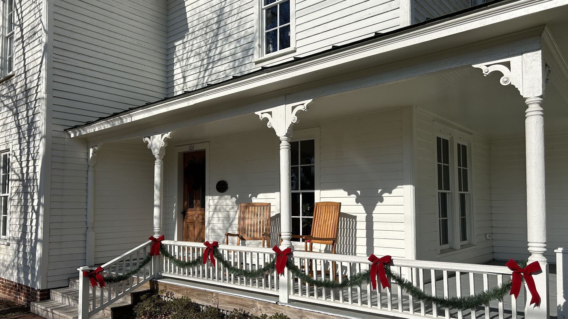 White house with porch. Green roping and red bows tied on porch railing.