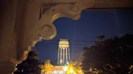 Water tower in background of town lit up at night. Corbel seen in top left corner.