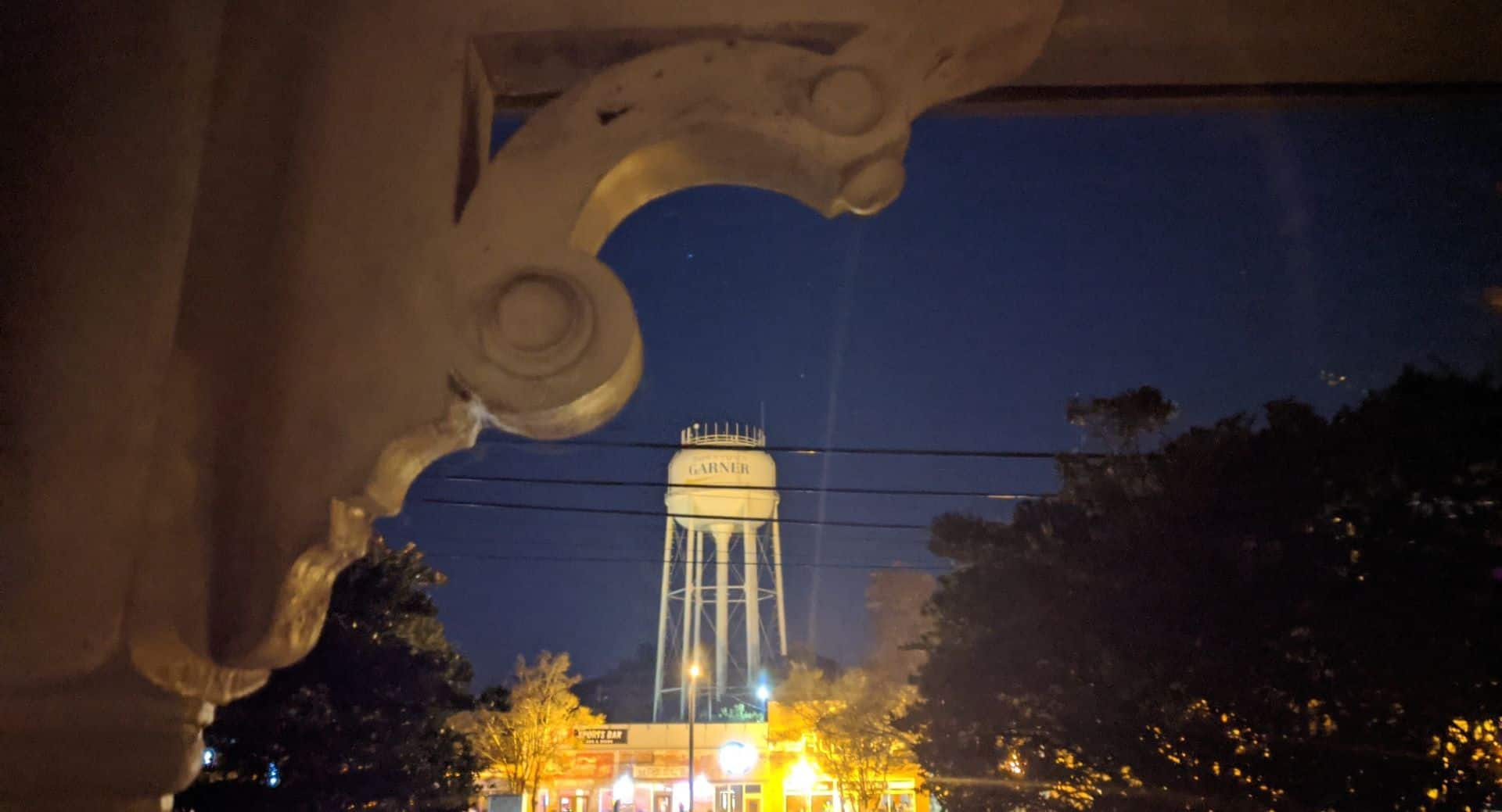 Water tower in background of town lit up at night. Corbel seen in top left corner.