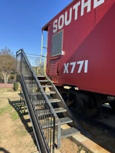 Black metal stairway beside a red caboose. 