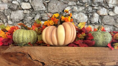 Green and orange pumpkins on wooden mantle. Rock background and some fall leaves of orange, red, and yellow.