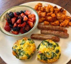 Mixed fruit, egg puffs, link sausage and sweet potatoes on a plate. 