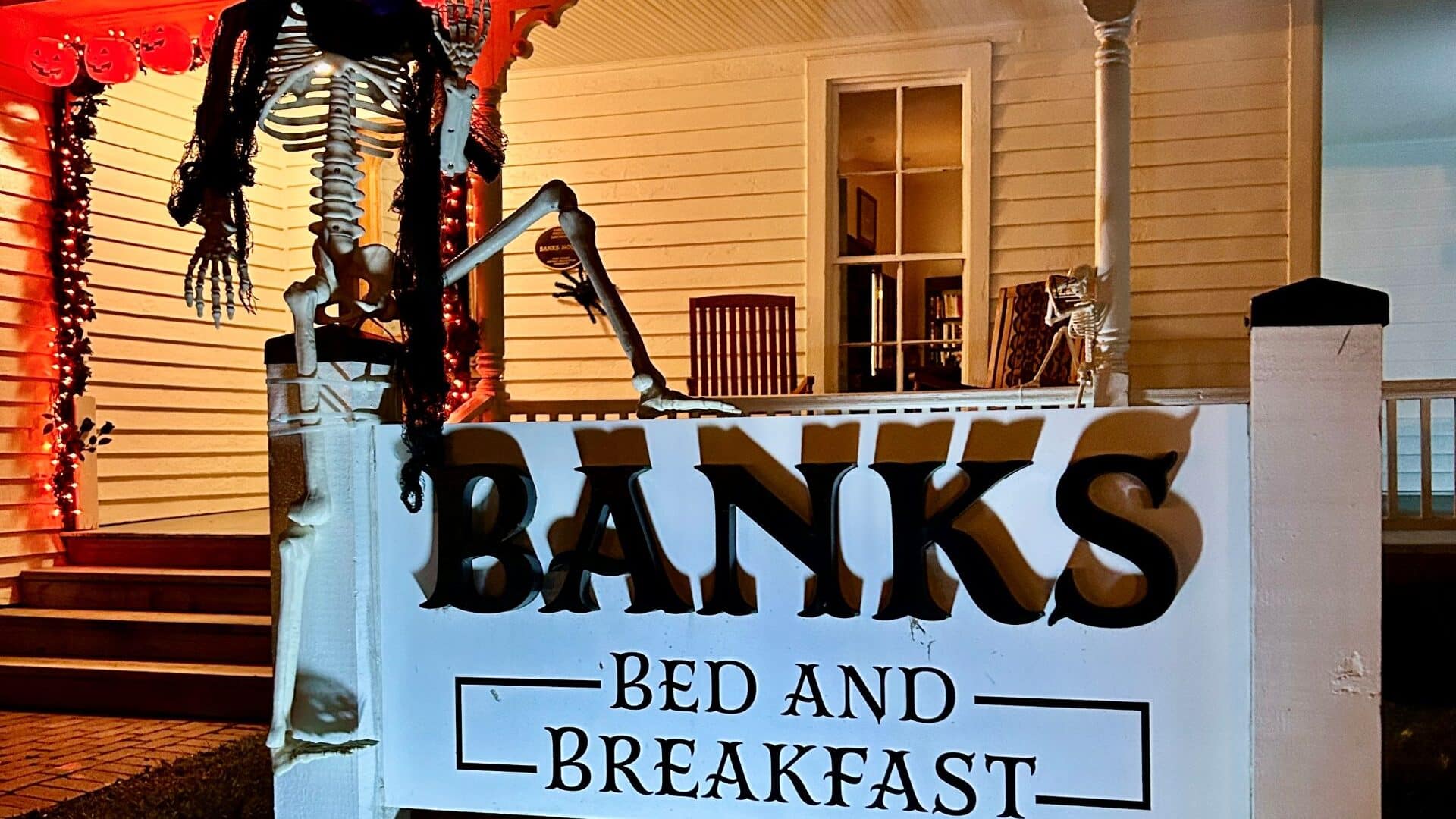 Skeleton sitting on a sign with rose in mouth and scarf around neck.