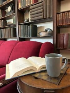 Red couch with bookshelf and books behind it. Coffee mug and book in front. 