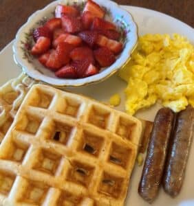 Red strawberries in a bowl on a plate with waffles, link sausage and eggs. 