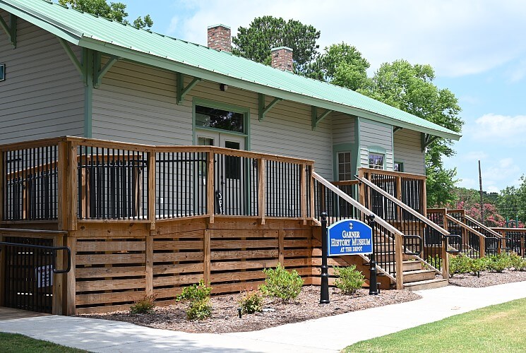 A small green building with green roof and trim, porch with a railing and blue business sign