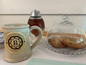 Tan mug on table by cookies covered with glass lid. 
