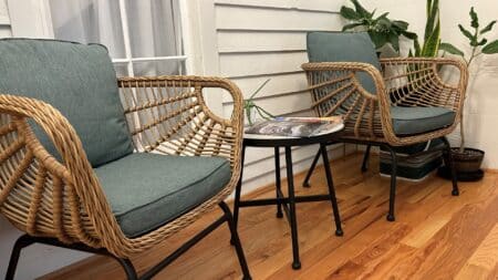 Wicker chairs with blue cushions and round table in the middle. Window in background