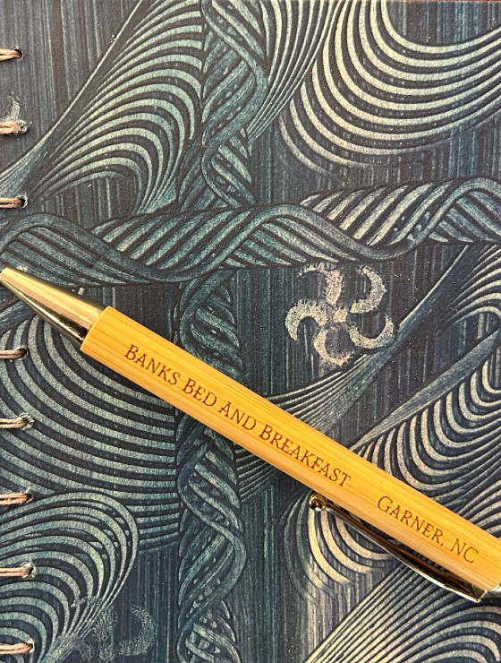 A wood and gold pen engraved with a business name sitting atop a patterned journal cover