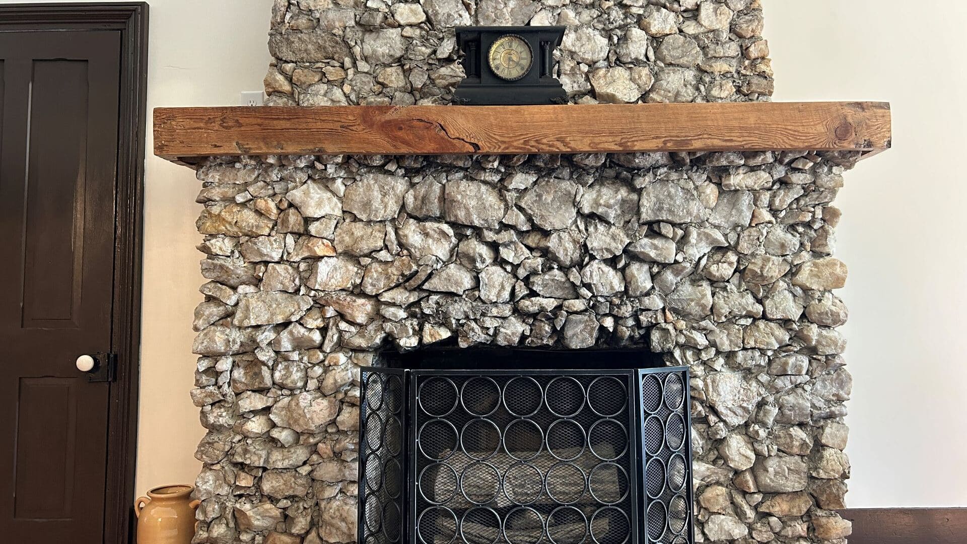 Fireplace covered in rock with wooden mantle and clock.