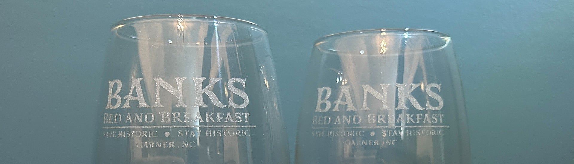 Two clear wine glassed etched with the logo of a bed and breakfast