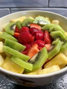 Red strawberries, green kiwis, and yellow pineapple cut up in a bow.