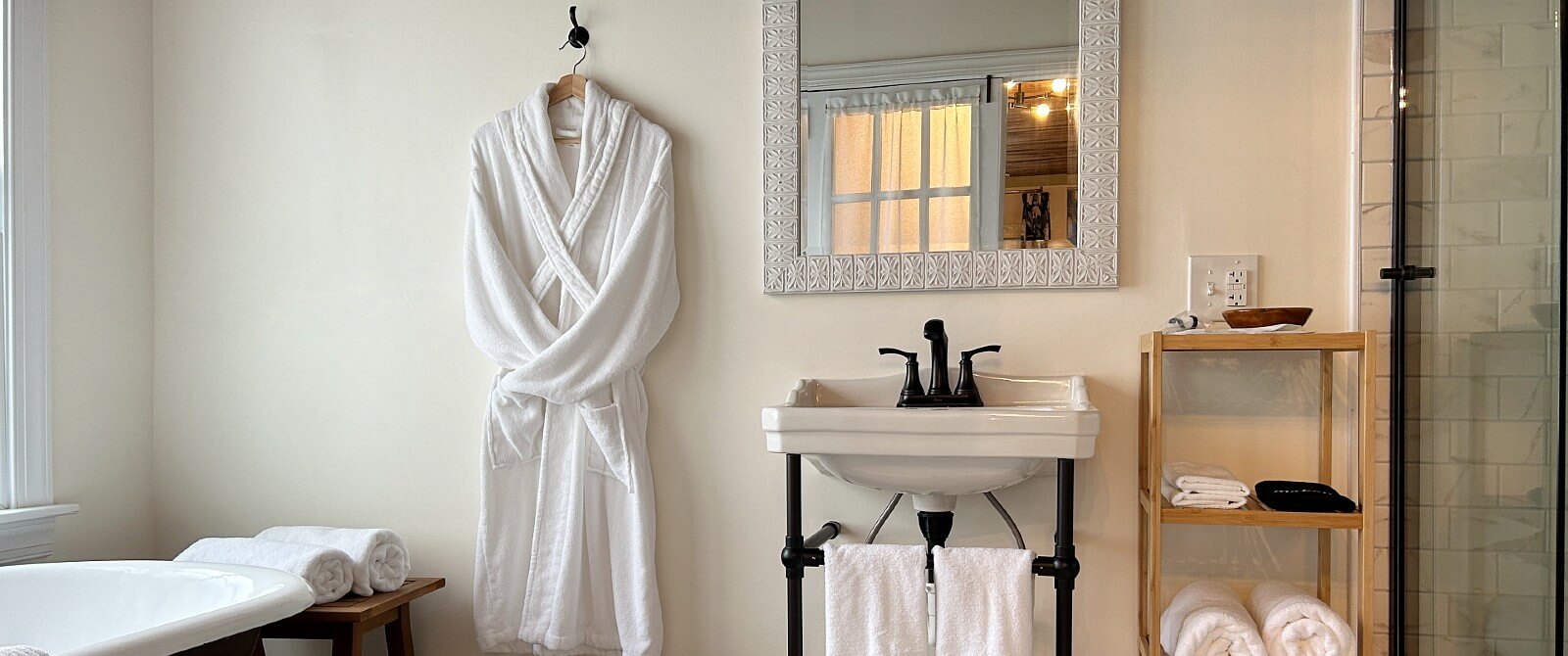 Bathroom with pedestal sink, clawfoot tub, hanging robe and wood shelf with towels