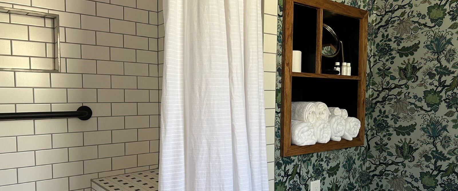 Bathroom with subway tiled shower, white curtain and built in cupboard surrounded by floral wallpaper