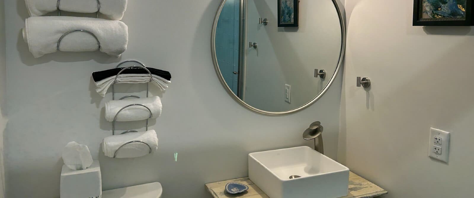 Bathroom with square table top sink, round mirror and silver racks with folded towels