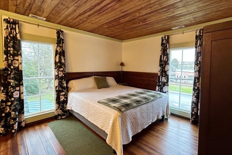 Spacious bedroom with queen bed, tall armoire and large windows with floral curtains