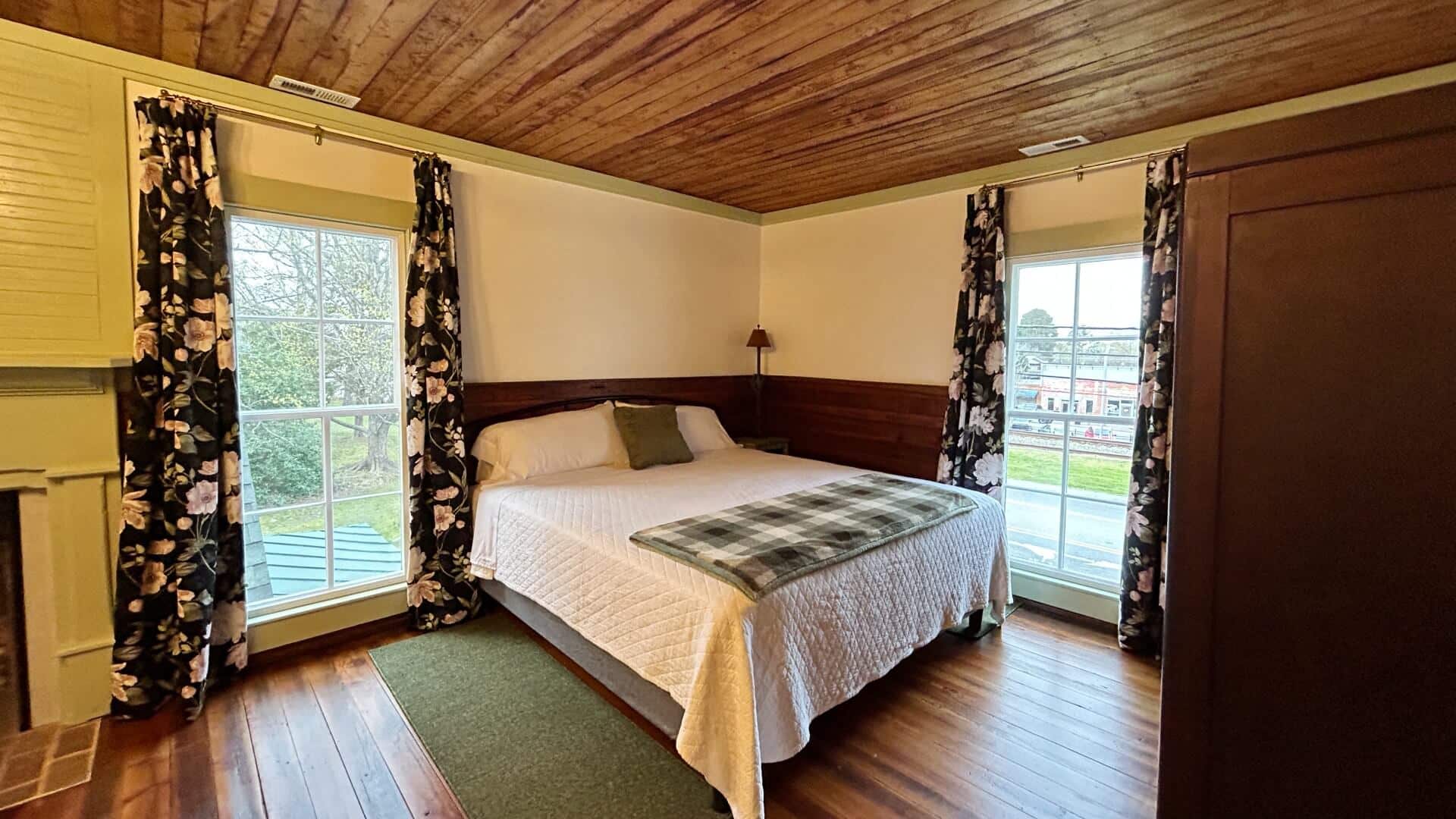 Spacious bedroom with queen bed, tall armoire and large windows with floral curtains