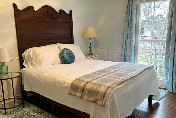 Guest room with queen bed with large antique headboard, side tables with lamps and large window with floral curtains