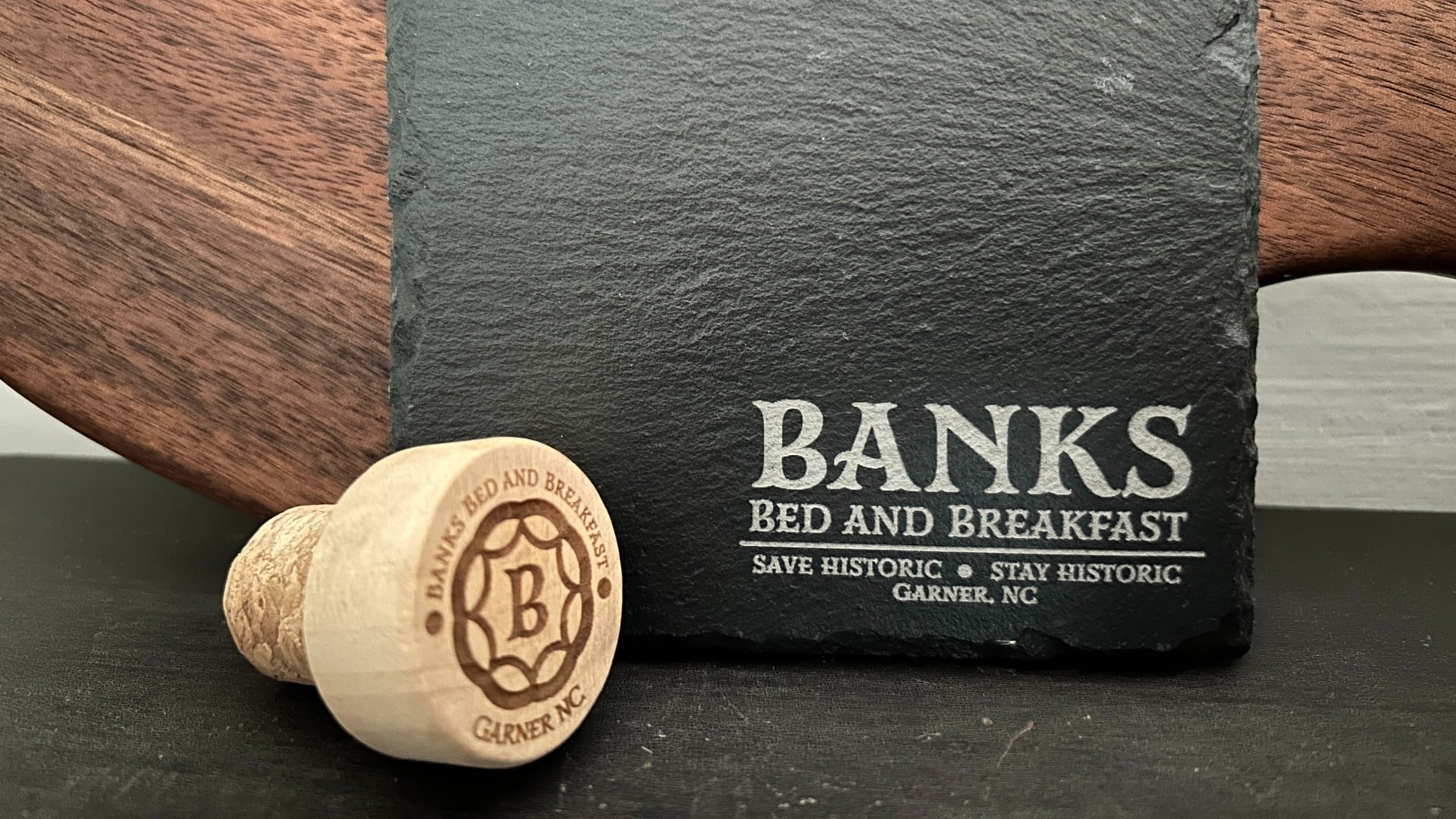 Wood platter with stone coaster and wine cork, both with the logo of a bed and breakfast