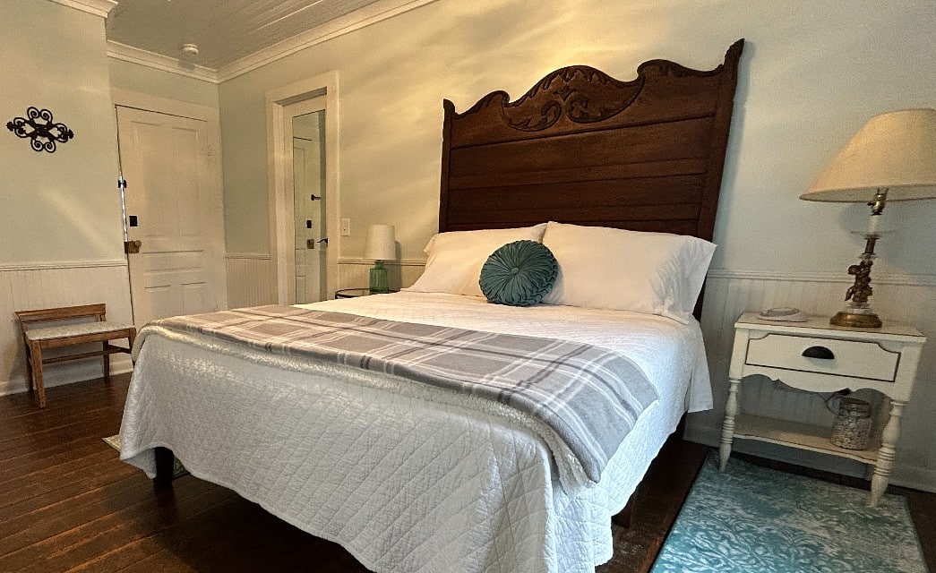 Guest room with queen bed with large antique headboard, side tables with lamps and hardwood floors