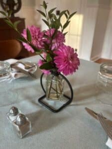 Pink flowers in vase on light green tablecloth. Salt and pepper shaker, white cloth napkins, and silverware around the edge.